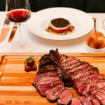 A steak on a cutting board with a glass of wine.