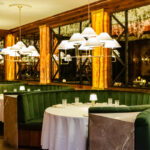The interior of a restaurant with green booths and chandeliers.