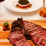 A steak on a wooden cutting board with a glass of wine.